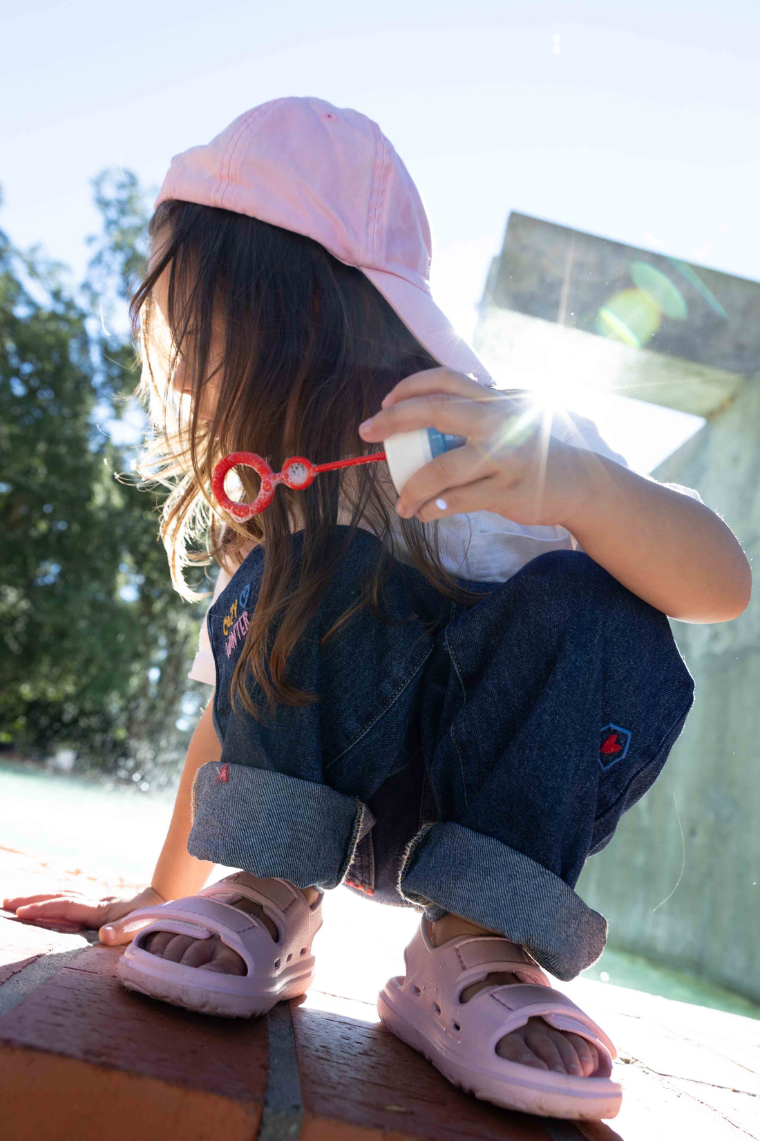 Close-up of light pink Wonderskips sandals worn by a child crouching outdoors, showing the flexible toe box and heel support.