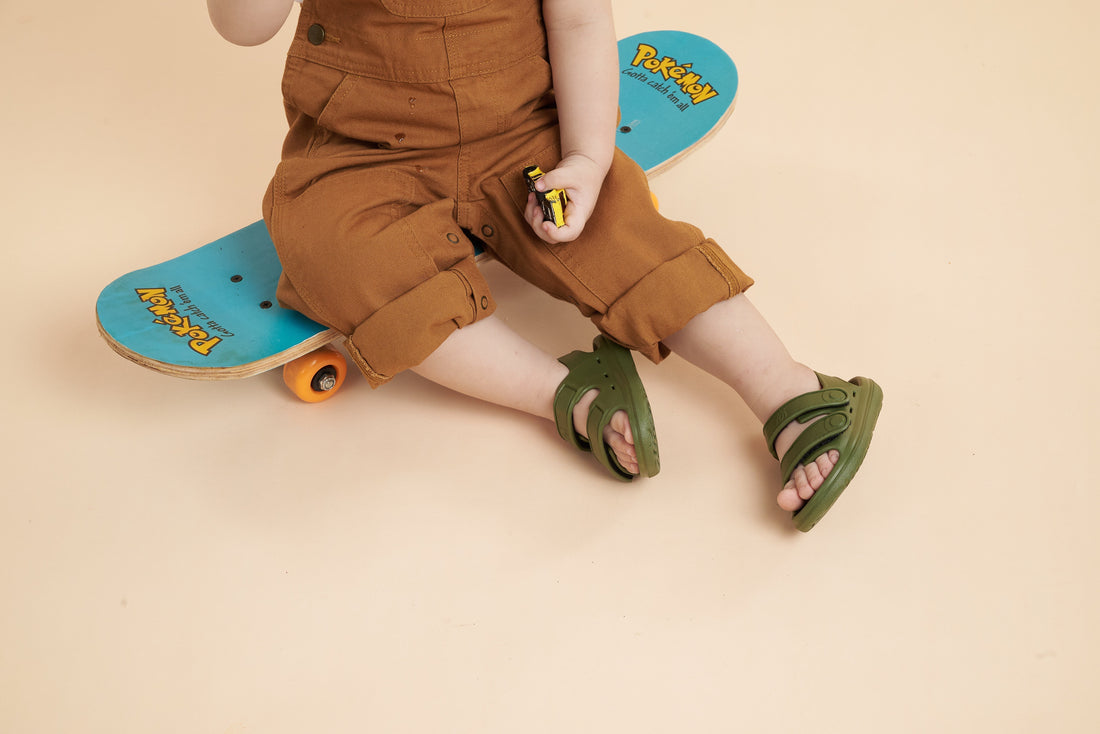 Child wearing green Wonderskips sandals sitting on skateboard, highlighting cushioned comfort and secure fit