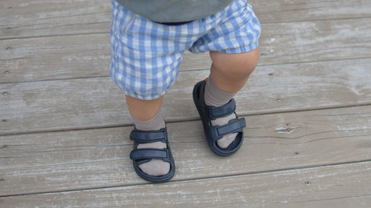 Toddler wearing navy Simples Wonderskip sandals with taupe socks