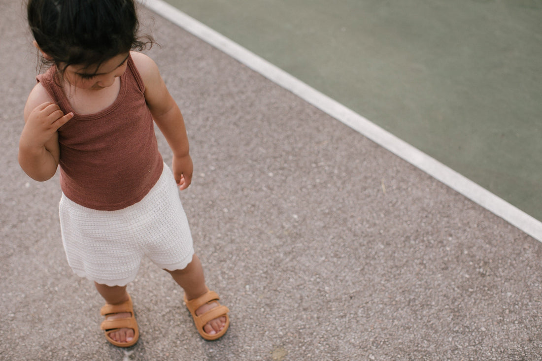 Wonderskips neutral-tone toddler sandals paired with a scalloped summer outfit on an outdoor playground.