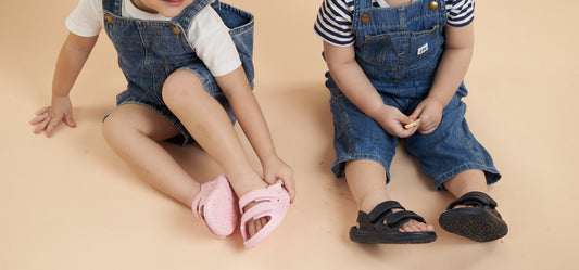 Two toddlers wearing WonderSkips sandals while sitting on the floor.