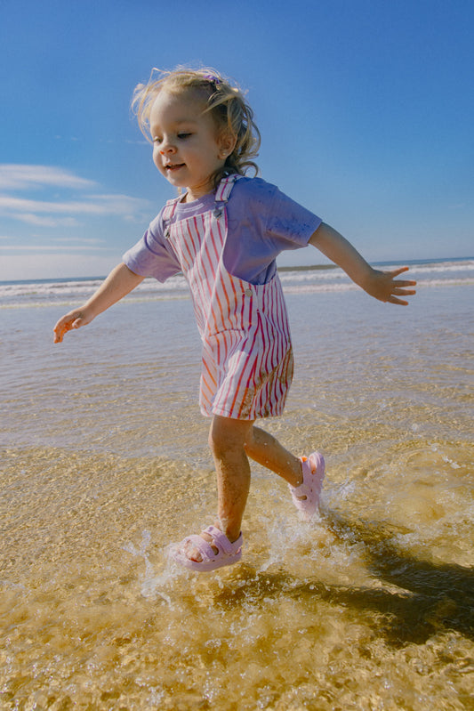 Young child running through ocean water wearing light pink Wonderskips waterproof sandals with secure heel straps.