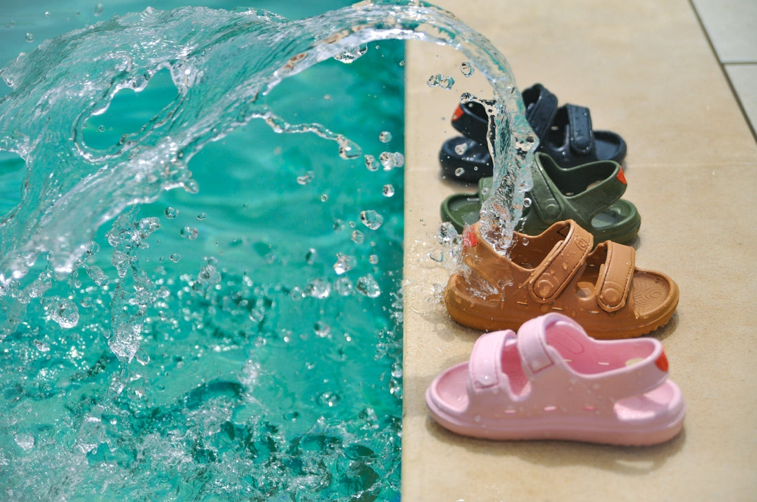Wonderskips waterproof toddler sandals in pink, tan, olive, and navy blue lined up by a swimming pool with splashing water.