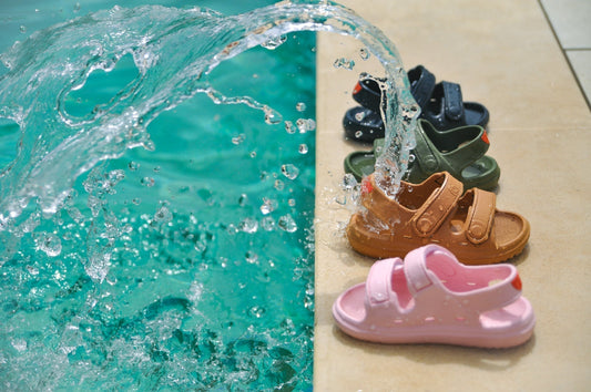 Wonderskips waterproof toddler sandals in pink, tan, olive, and navy blue lined up by a swimming pool with splashing water.