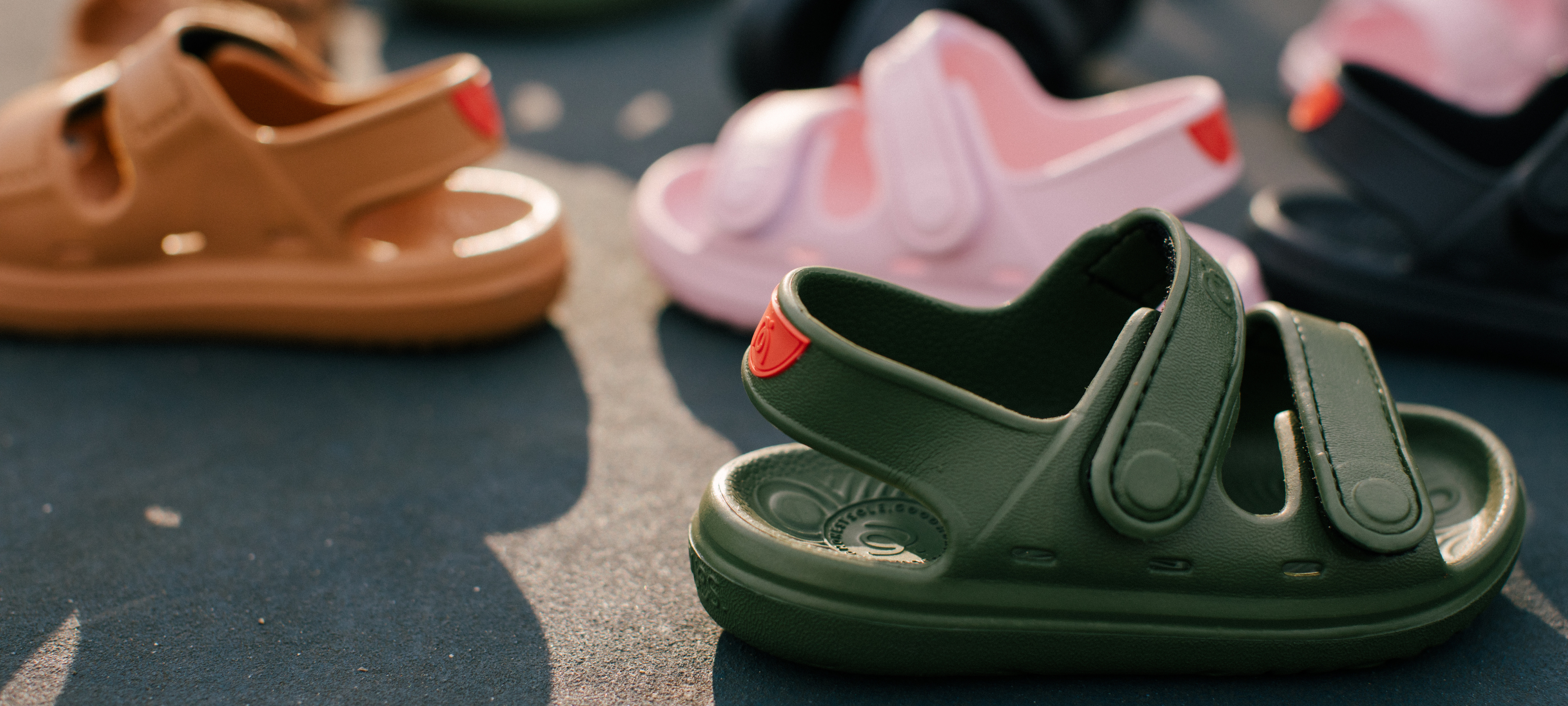Simples Wonderskip Green children's sandals with red accents on a dark surface